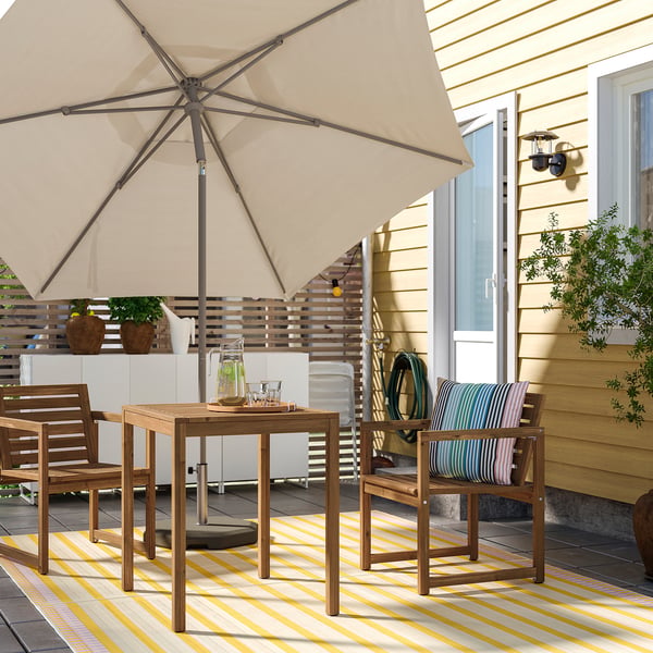 Patio confortable avec parasol, table, chaises et tapis à côté d’une maison jaune.