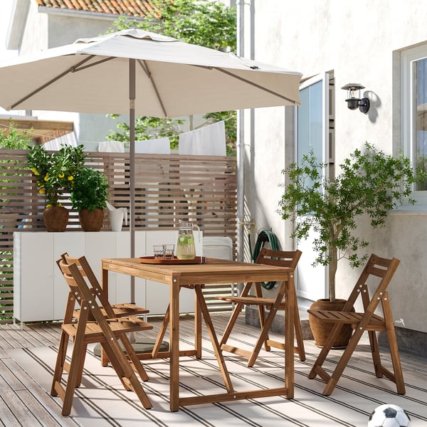 Ensemble de patio en bois avec parasol sur la terrasse. Quatre chaises, des plantes et une maison en arrière-plan.
