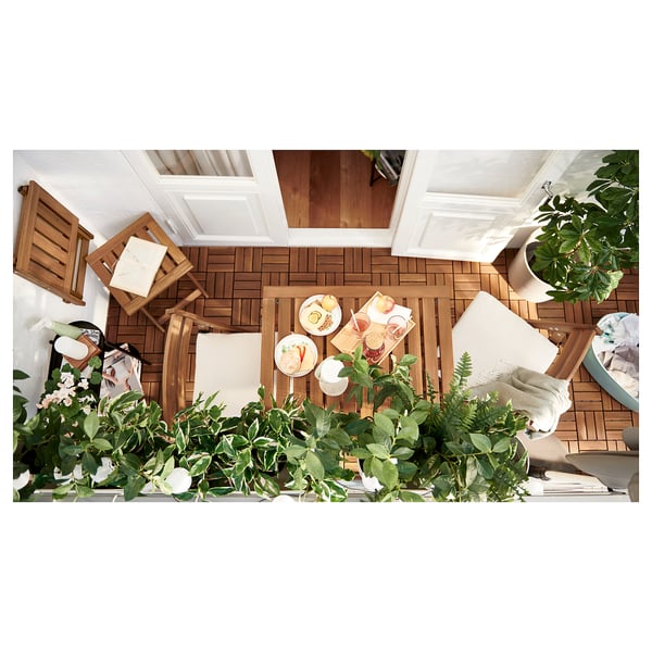 Table d’extérieur en bois avec coussins, nourriture et plantes sur un balcon.