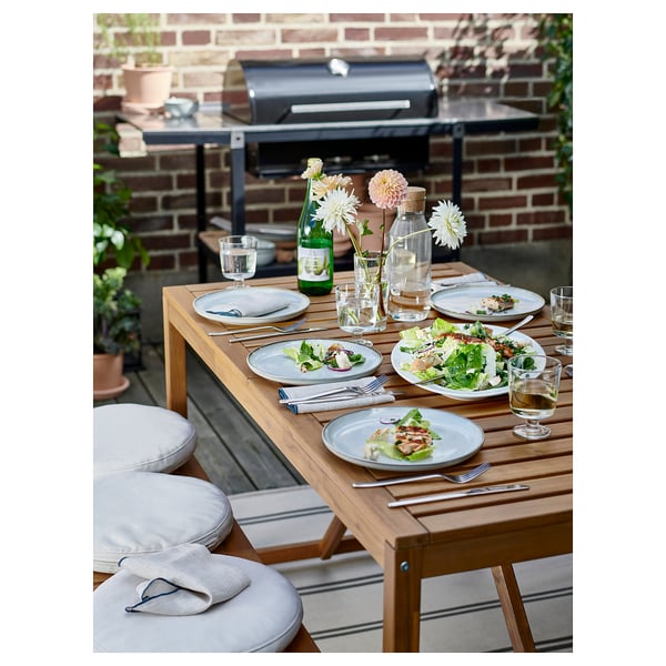 Configuration de salle à manger en plein air avec table et chaises NÄMMARÖ, y compris des assiettes, des verres, des couverts, de la salade et un grill.