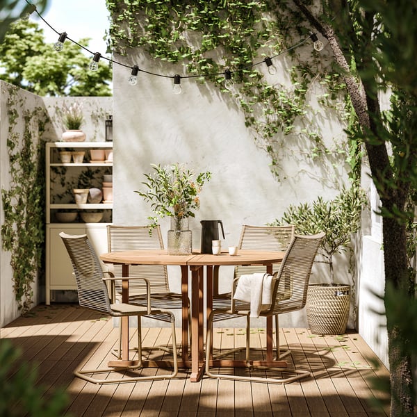 Ensemble de patio extérieur avec table ronde en bois et chaises noires sous des guirlandes lumineuses.