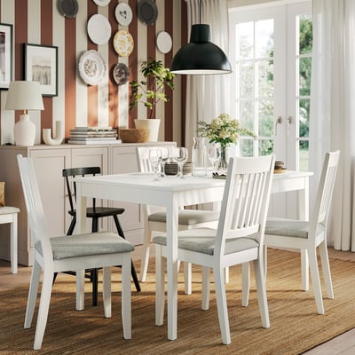 Table à manger blanche avec 4 chaises grises, extensible, décorée d’assiettes, de lampe, de livres et de vases.