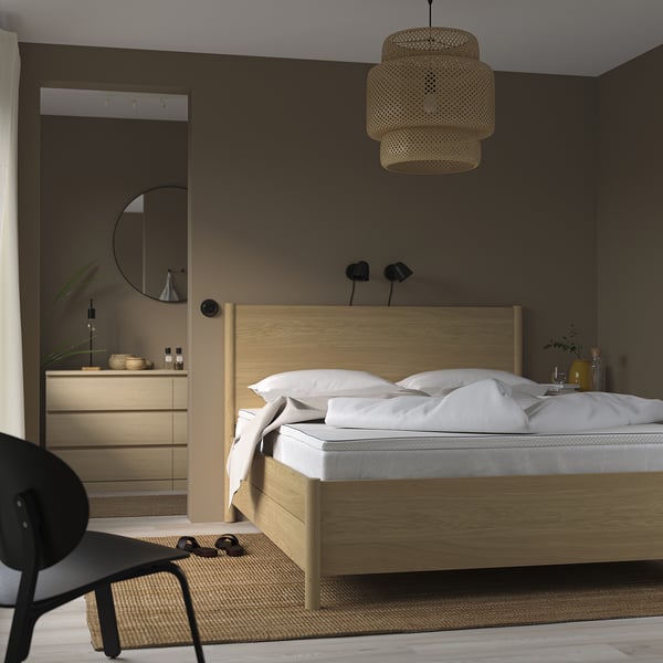 Chambre minimaliste avec lit en bois, tables de chevet, chaise noire et lampe suspendue.