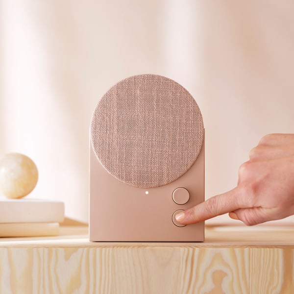 Touche de la main bouton sur haut-parleur bluetooth beige sur étagère en bois.