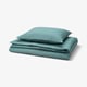 Un ensemble de literie bleu-vert plié, avec une couette et des taies d’oreiller à rayures subtiles, soigneusement empilées, mettant en valeur son tissu lisse et satiné.