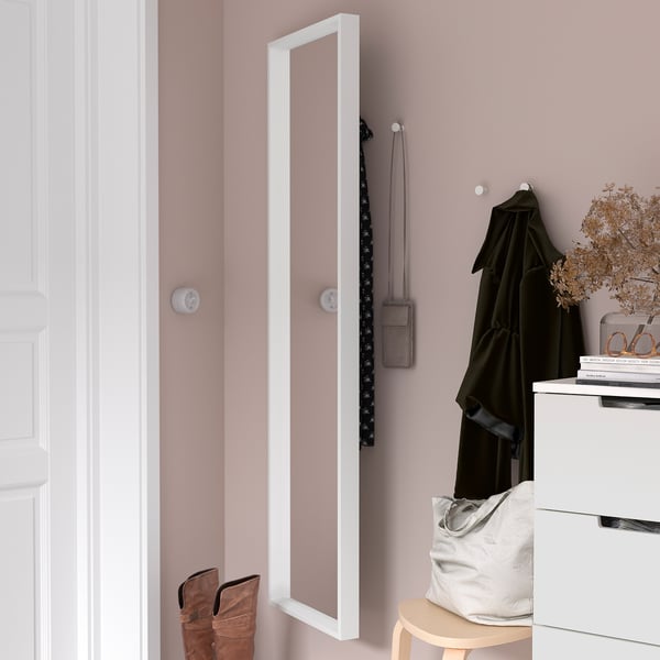Une armoire à miroir sur un mur rose avec patère. En dessous, un tabouret contient un sac et des bottes, à côté d’un tiroir avec des livres et des fleurs séchées.