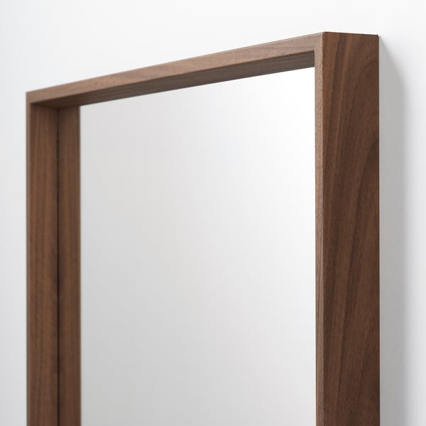 Un miroir à cadre en bois de haute qualité aux lignes épurées, monté sur un mur, reflétant une surface lumineuse et claire.