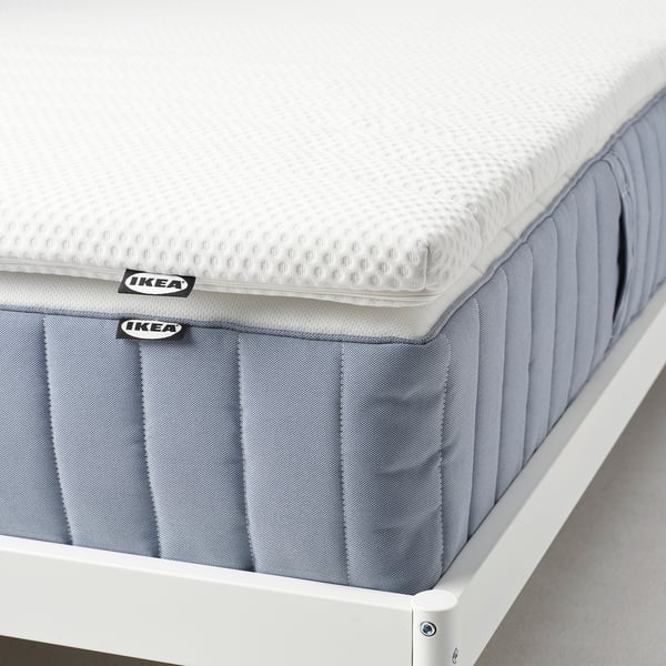 Un surmatelas IKEA NISSEHOLM exposé, doté d’une base en mousse grise haute résilience et d’une couche supérieure blanche et texturée pour un soutien plus ferme.