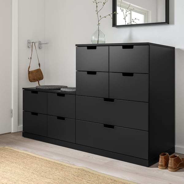 Coffre noir NORDLI avec deux unités, offrant un grand espace de rangement. Design minimaliste avec tapis, sac et plante.