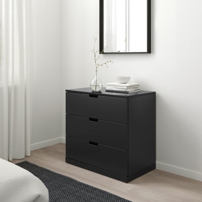 Commode moderne à 3 tiroirs NORDLI noir, élégante et minimaliste, s’adapte aux espaces compacts. Bien placé sous un miroir, avec un grand rideau blanc à proximité.