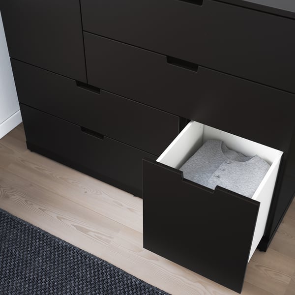 Commode noire avec un tiroir ouvert, révélant des vêtements gris pliés. Les tiroirs ont des mécanismes de fermeture lisses et douces.