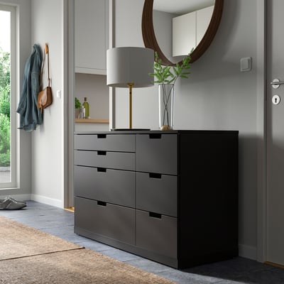 Coffre NORDLI moderne gris foncé avec miroir, lampe, plante et patère.