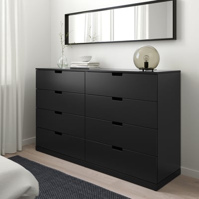 Commode moderne NORDLI avec miroir, lampe et tiroirs entre la fenêtre et le lit.