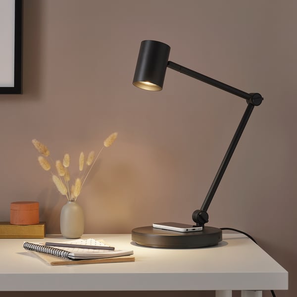 Lampe NYMÅNE sur bureau blanc avec des livres, des fleurs et une boîte orange.