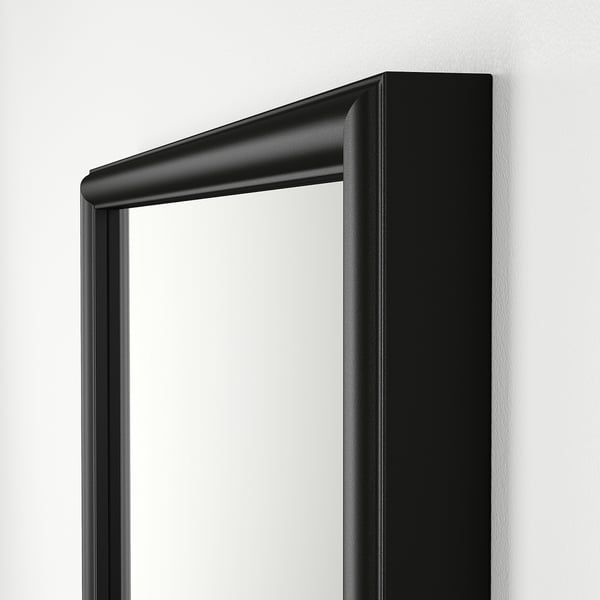 Miroir élégant et moderne à cadre noir avec des bords lisses, monté sur un mur clair.
