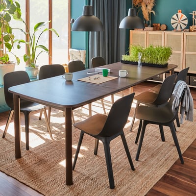 Salle à manger confortable avec des chaises grises modernes et une table extensible, des lampes suspendues, des plantes et un décor naturel.