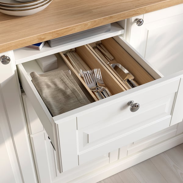 Tiroir de cuisine blanc ouvert avec range-couverts et serviettes pliées, montrant un rangement organisé.
