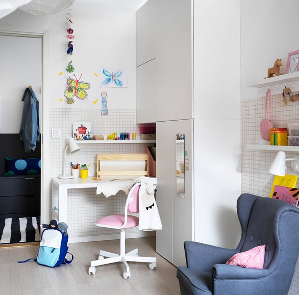 Chambre d’enfant avec des murs blancs, une chaise bleue, un petit bureau, des étagères et des décorations colorées.