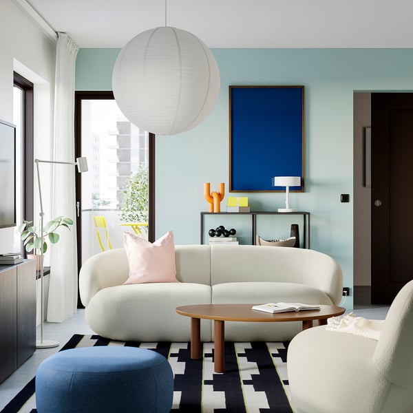 Salon moderne avec murs bleus, canapé blanc, table basse en bois, lampe suspendue et œuvres d’art bleues.