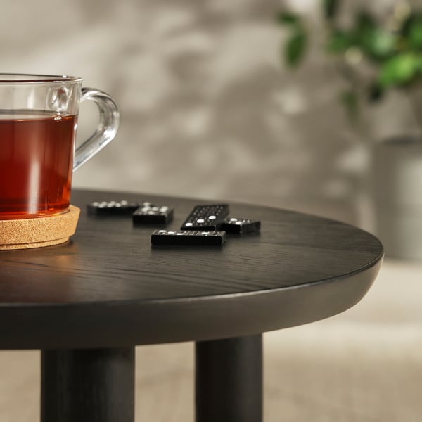 Une tasse en verre remplie de thé repose sur une table en bois sombre à côté de télécommandes noires.