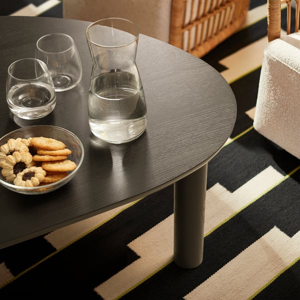 Äopy : table ronde avec lunettes, bol à biscuits, sur tapis rayé. Bois foncé, design minimaliste.