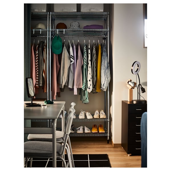 Armoire moderne avec cintres, étagères et chaussures dans un placard organisé. Cadre en métal argenté, vêtements colorés et tiroirs de rangement noirs.
