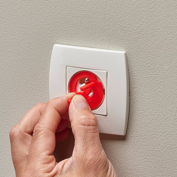 Une main enfonce une fiche de sécurité rouge à l’épreuve des enfants dans une prise murale blanche, assurant ainsi la sécurité électrique des enfants.