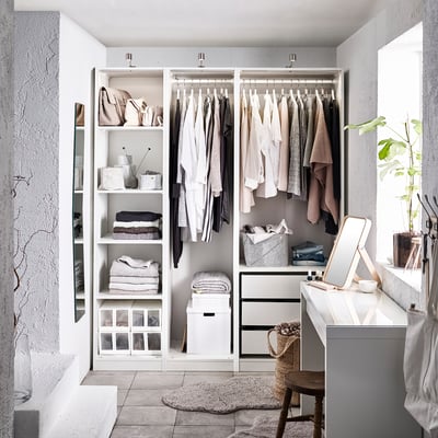 Armoire blanche moderne avec vêtements, étagères et tiroirs. Un miroir et une plante à côté.