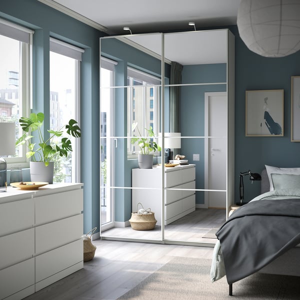 Chambre moderne dotée d’armoires PAX blanches avec portes coulissantes en miroir, d’une literie grise, de murs bleu-vert et de parquet avec un tapis tissé.
