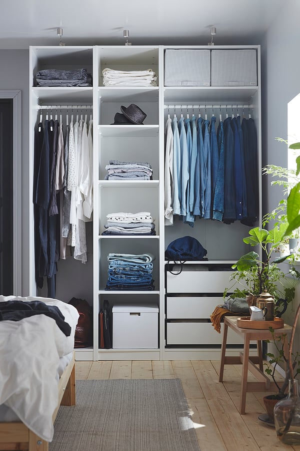 Chambre moderne avec armoire PAX blanche, vêtements bleus, parquet et plantes vertes.