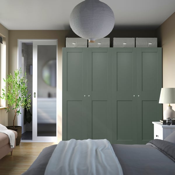 Chambre moderne avec grande armoire bleu sarcelle, boîtes grises et porte de salle de bain ouverte. Lit au premier plan.