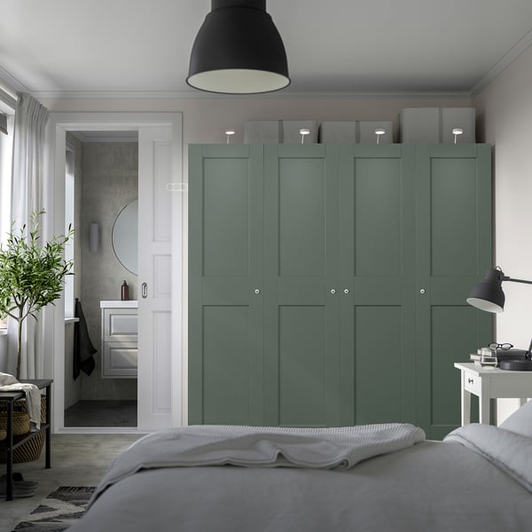 Chambre moderne avec grande armoire PAX verte, design minimaliste, rangement gris, vue partielle sur le lit, salle de bain adjacente avec miroir circulaire.
