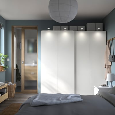 Chambre moderne avec une armoire PAX blanche, une literie grise et une porte d’accent en bois.