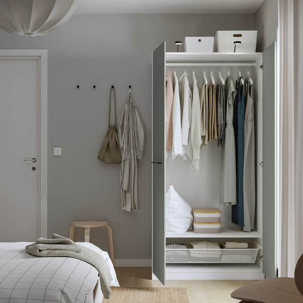 Armoire moderne avec cintres, couvertures et bacs de rangement. Manteaux sur crochets à côté d’une porte.