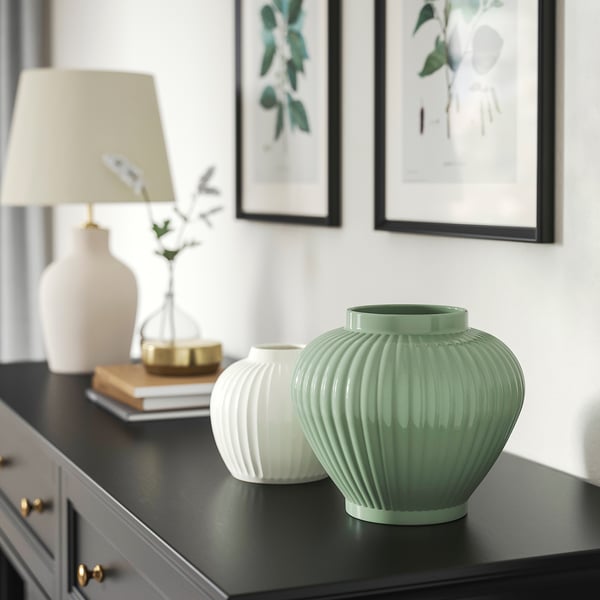 Vases PELARBJÖRK gris-vert sur étagère noire avec livres, lampe et décor doré. Le vase vert plus grand contraste avec le plus petit vase blanc.