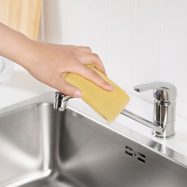 Nettoie à la main le robinet de la cuisine avec une éponge jaune.