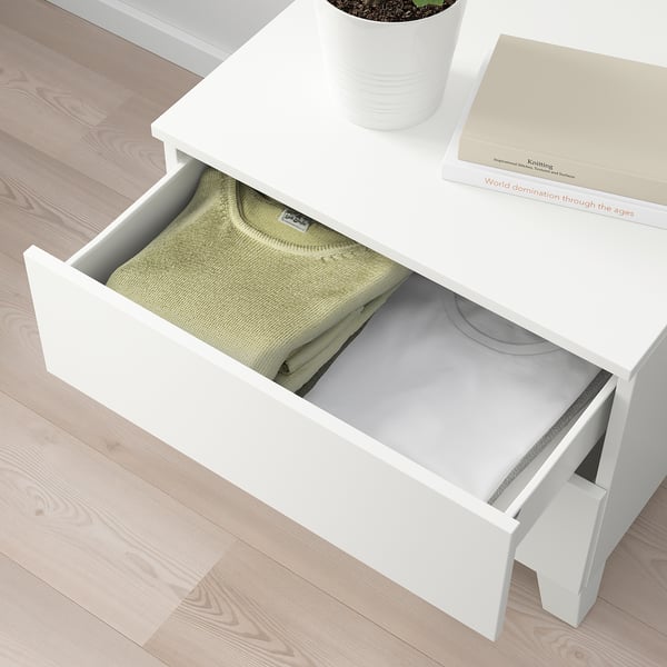 Unité de rangement PLATSA blanche avec tiroir ouvert contenant des vêtements, un livre et une plante.