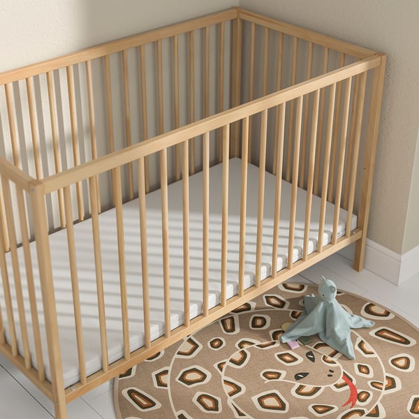 Matelas pour bébé en mousse PLUTTIG, beige clair, rectangulaire, s’adapte parfaitement au lit d’angle, doux et sûr, tapis et jouet assortis à proximité.