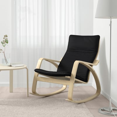 Salon moderne avec fauteuil à bascule en cuir noir, lampadaire et vase de fleurs.