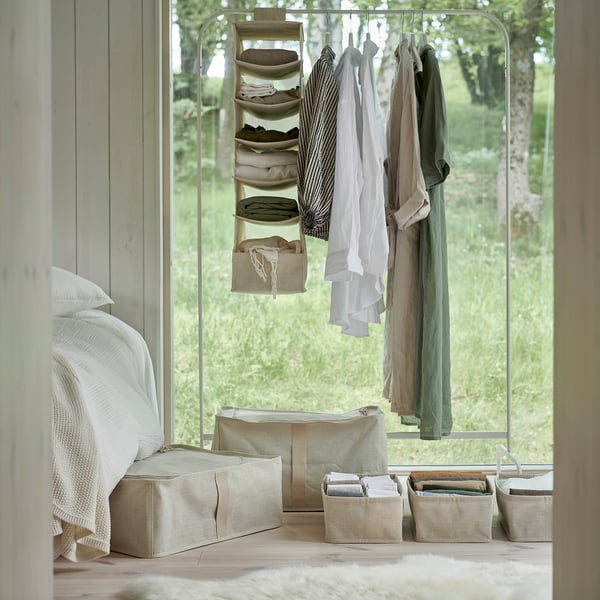 Chambre à coucher avec organisateur de vêtements PURRPINGLA et étuis de rangement beiges. Design épuré et minimaliste avec un lit et une fenêtre verdoyante.