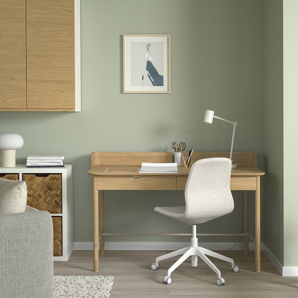 Configuration minimaliste du bureau à domicile avec bureau RIDSPÖ, chaise en bois clair et blanc, mur vert, petite impression d’art, scrivani soigneusement organisé.
