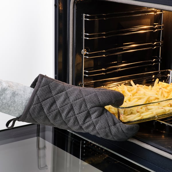 Personne portant des gants gris RINNIG plaçant un plateau d’aliments dans le four. Les gants protègent les mains de la chaleur.