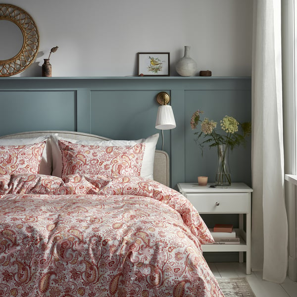 Chambre confortable avec tête de lit turquoise, literie blanche, motifs floraux, miroir, vase, fleurs et lampes.