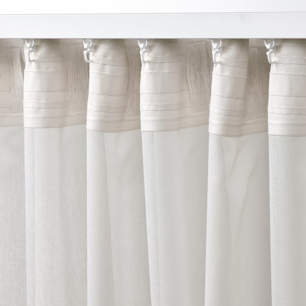 Des rideaux transparents blancs avec des dessus plissés pendent gracieusement, permettant une lumière filtrée et assurant l’intimité.