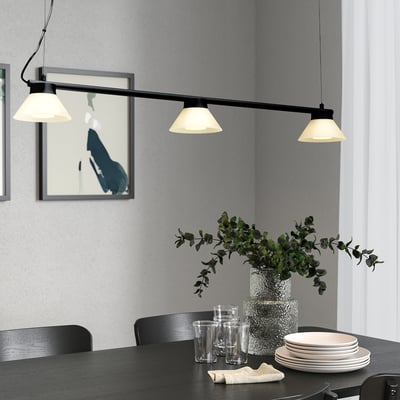 Salle à manger moderne avec lampe SAMBORD au-dessus d’une table avec verres, assiettes et verdure. Design élégant et minimaliste avec beaucoup de lumière.