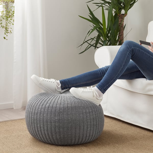 La personne se détend sur un canapé sectionnel blanc, reposant les pieds sur un pouf SANDARED tricoté gris, qui sert de repose-pieds.