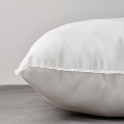 Gros plan d’un oreiller blanc et dodu sur un lit, mettant en valeur sa texture douce et ses coutures précises.