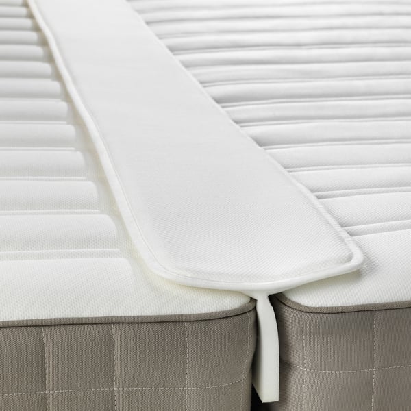 L’image représente un remplisseur d’espace de matelas blanc, fixant un pli entre deux matelas.