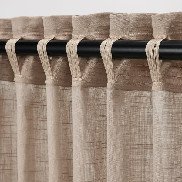 Des rideaux simlerönn beiges avec texture en lin pendent d’une tige noire, montrant un design plissé pour l’intimité et le filtrage de la lumière.