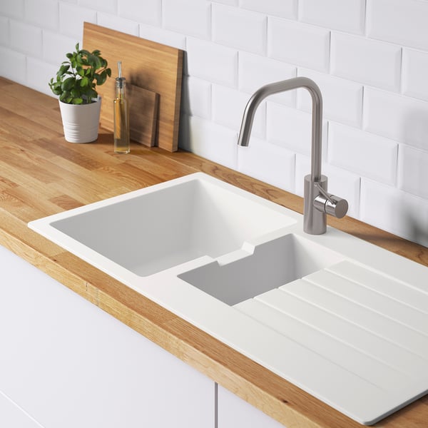 Évier de cuisine blanc avec comptoir en bois, robinet métallique, plante verte et bouteille d’huile.